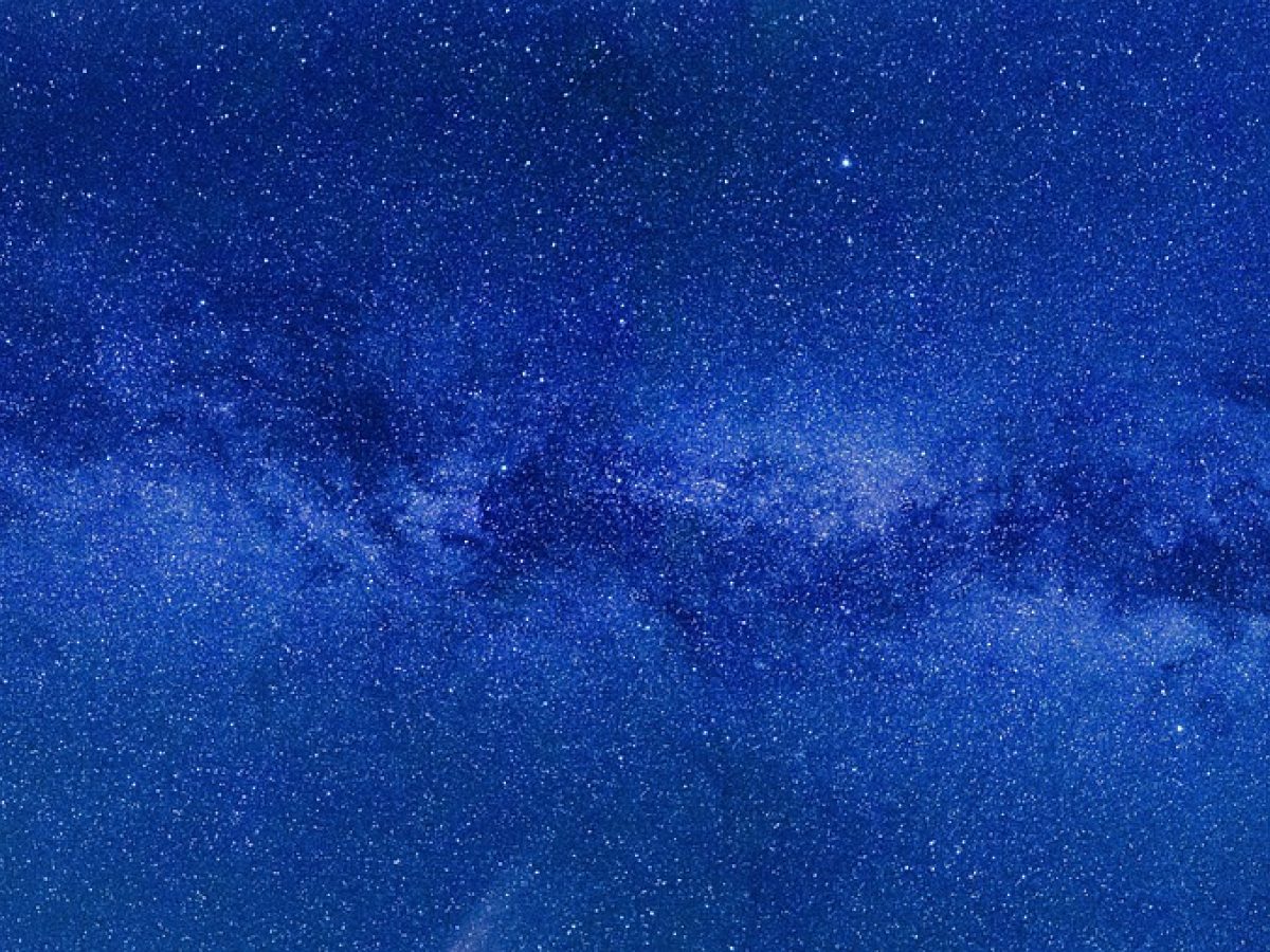 星空品牌关于页配图：深青色夜空下银河横贯山脊线，一位观测者背着三脚架静立远望，远处帐篷透出暖光，整体氛围安静辽阔