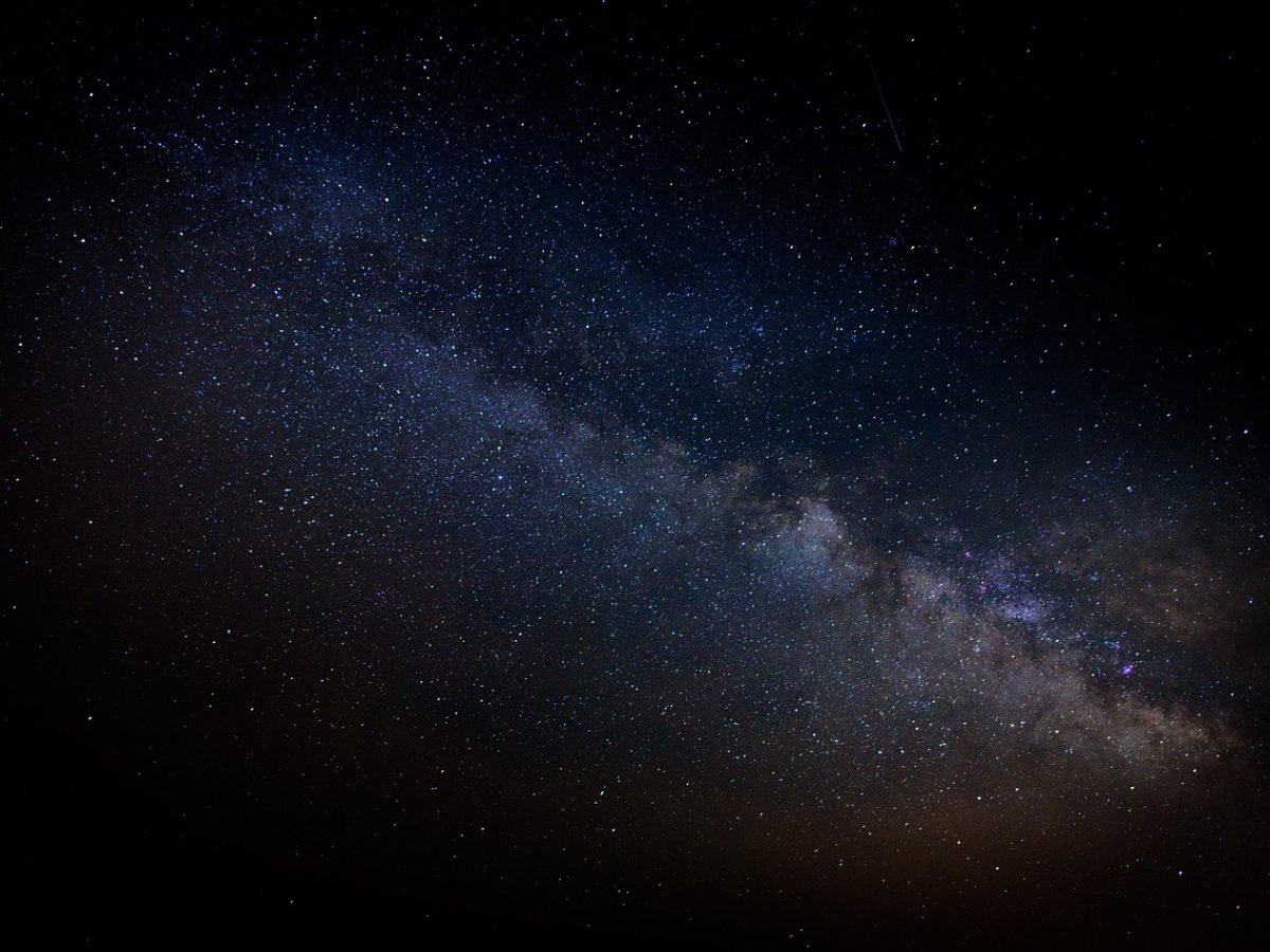 星空 深蓝夜空下银河横贯山脊，两位观星者站在草坡上举起双筒望远镜仰望，远处地平线泛着微弱暖光